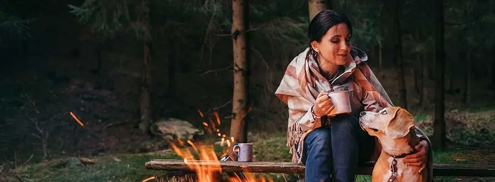 A dog and its owner sitting by a campfire