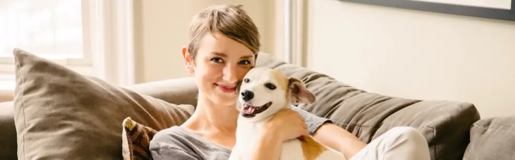 A dog and its owner smiling while cuddled on the couch