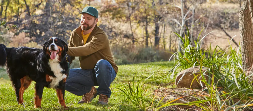 a man squatting next to his dog out in nature